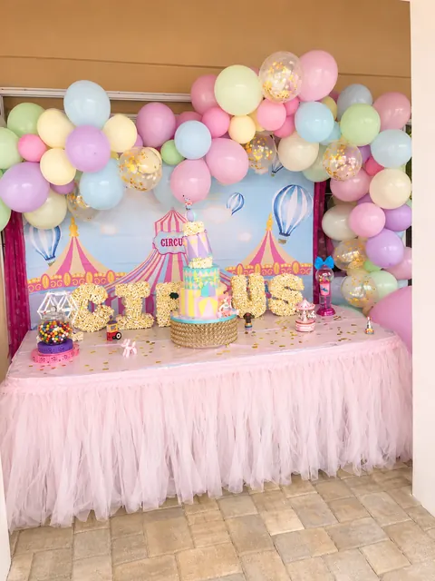 Pastel circus dessert table with a pink tulle skirt and balloon garland
