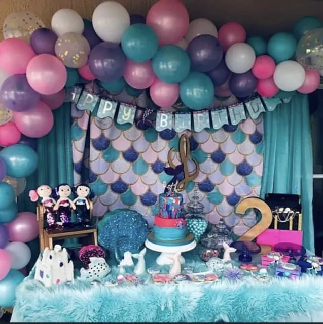 Pink, purple and teal balloon garland over a mermaid-scale backdrop and dessert table