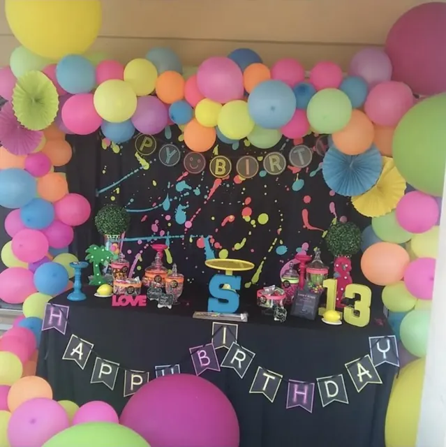 Neon balloon garland around a paint-splatter backdrop and candy table for a 13th birthday